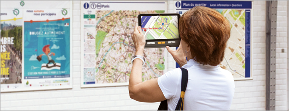 La photo représente une dame utilisant la loupe Explorer 8 devant un plan de métro